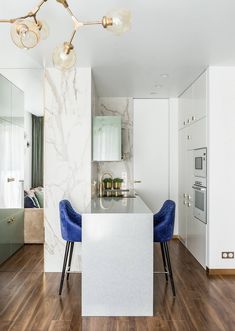 a modern kitchen with marble counter tops and blue chairs in front of an island that is surrounded by wood flooring