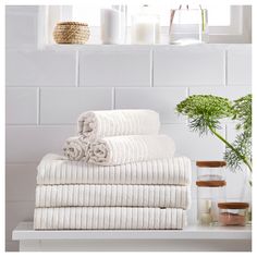 a stack of towels sitting on top of a white table next to a vase with flowers