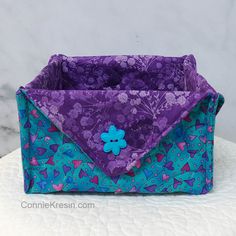 a purple and blue bag with a flower on the front sitting on a white surface