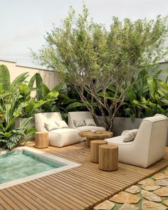 a wooden deck with chairs and tables next to a pool surrounded by greenery on the other side