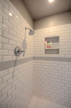 a bathroom with white tile and gray grouting on the walls, shower head, and hand held faucet