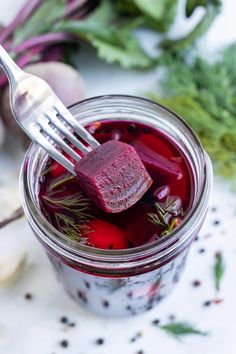 a fork in a jar filled with beets and other vegetables next to some herbs