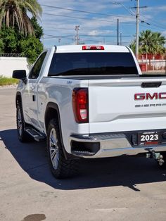 the back end of a white truck parked in a parking lot with palm trees behind it