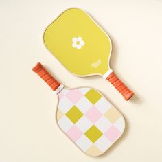 two wooden paddles with colorful designs on them, one yellow and the other pink