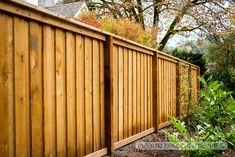 a wooden fence next to a lush green tree and shrubbery in front of a house