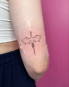 a small bat tattoo on the left side of the right arm is shown in black ink