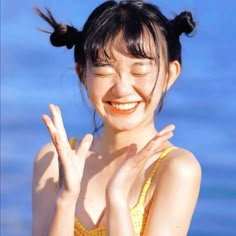 a woman in a yellow bathing suit holding her hands up to the side and smiling