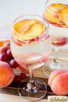 two glasses filled with liquid and fruit on a wooden tray next to some peaches