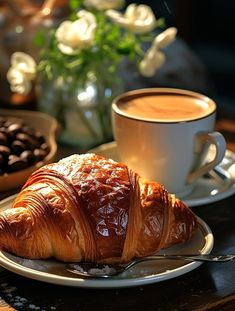 a croissant on a plate next to a cup of coffee and chocolate beans