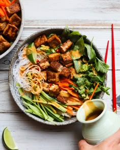 a bowl filled with tofu and vegetables next to chopsticks on a table