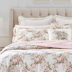 a white bed with pink flowers on it and two framed pictures above the headboard