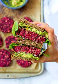 a person is holding up a sandwich with beets and avocado