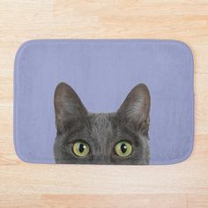 a gray cat with green eyes on a blue mat in front of a wooden floor