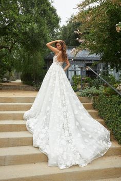 a woman in a white wedding dress standing on steps with her hands behind her head