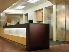 an empty reception area with wood flooring and lights on the ceiling, along with a large wooden counter