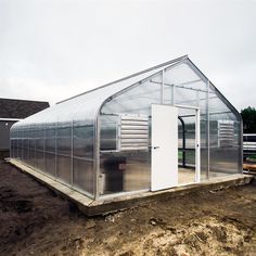 a small greenhouse in the middle of a dirt field with a white door on it