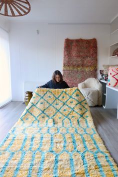 a woman is sitting on the floor in front of a large yellow and blue rug