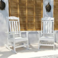 two white rocking chairs sitting next to each other in front of a wall with wooden shutters