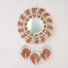 a round mirror with tassels hanging from it's sides on a wall