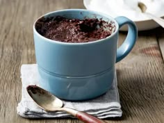 a blue mug filled with chocolate cake sitting on top of a wooden table next to a spoon