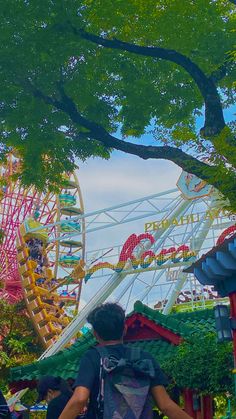 a man is standing in front of a ferris wheel at an amusement park with trees