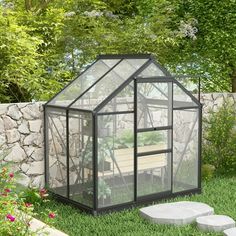 a small green house sitting on top of a lush green field next to a stone wall