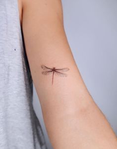 a woman's arm with a small dragonfly tattoo on it