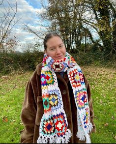 a woman wearing a multicolored crochet scarf in the grass with trees in the background