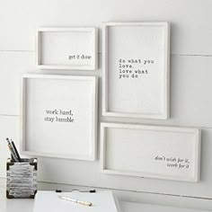 three white framed pictures on the wall above a desk with a pen and pencil holder