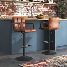 two brown leather barstools sitting in front of a brick wall and counter top