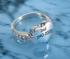 a close up of a diamond ring on a marble surface with the name dad written on it