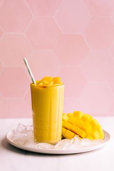 a mango smoothie on a white plate next to sliced mangoes with a straw