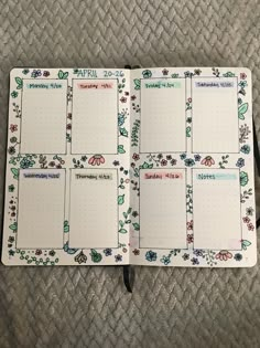 an open planner with flowers on it sitting on top of a bed next to a pen