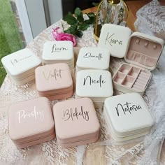 six small boxes with names on them sitting on a lace covered tablecloth next to a pink flower