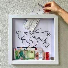 a person's hand is holding a piece of paper and money in a shadow box