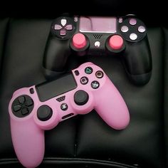 two video game controllers sitting next to each other on a black leather surface with pink and white buttons