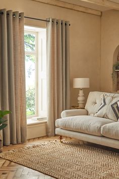 a living room filled with furniture and a large window covered in curtains next to a rug