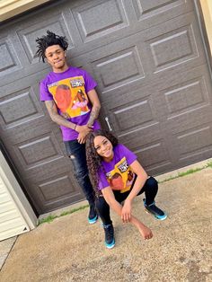 two people standing next to each other in front of a garage door wearing matching shirts