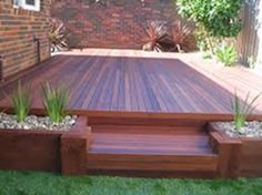 a wooden deck surrounded by plants and rocks in the grass next to a brick building