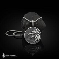 a pendant with a dolphin head on it sitting next to a black rock and water