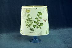 a lamp shade with green leaves and butterflies printed on it, sitting on a blue surface