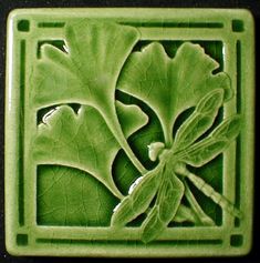 a green ceramic tile with a dragonfly on it's back and leaves in the center