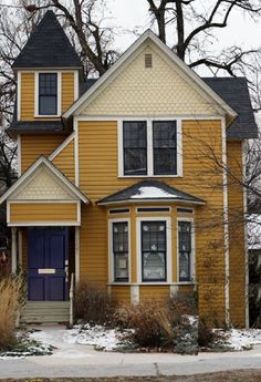 a yellow two story house with blue door and windows in the snow covered front yard