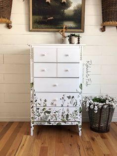 a white dresser with flowers painted on it in front of a painting and two baskets