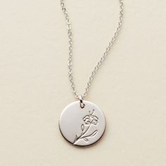 a silver necklace with a flower on the front and a small white disc in the middle