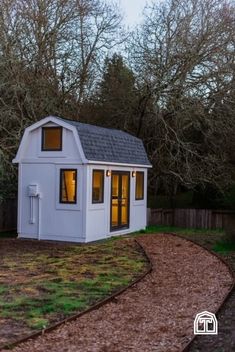 a small white shed sitting on top of a lush green field next to a forest