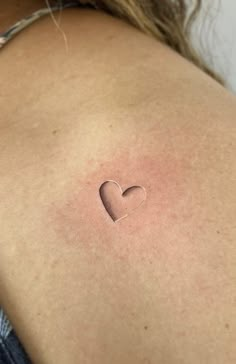 a woman's back with a small heart tattoo on her left shoulder and chest