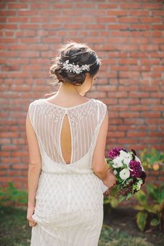 the back of a bride's dress with flowers in her hair, holding a bridal bouquet