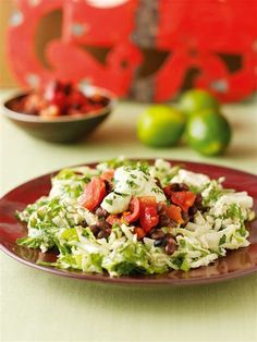 a red plate topped with lettuce and tomatoes next to bowls of limes