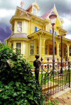 a large yellow house sitting on top of a lush green field next to a tall metal fence